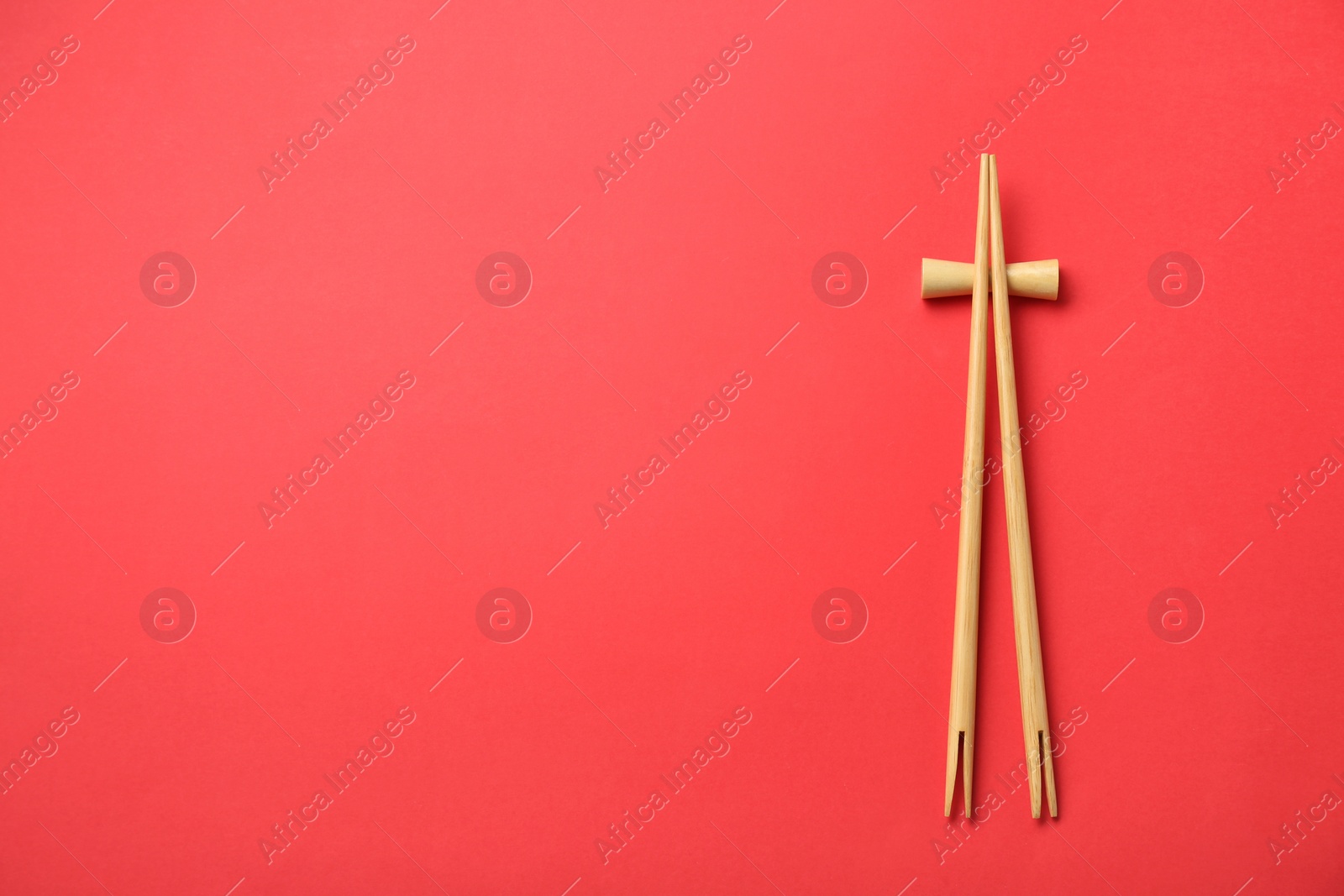 Photo of Pair of wooden chopsticks with rest on red background, top view. Space for text