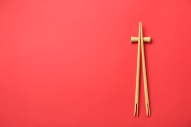 Photo of Pair of wooden chopsticks with rest on red background, top view. Space for text