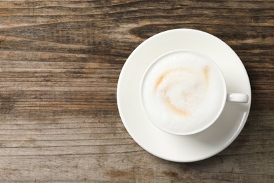 Photo of Tasty cappuccino in coffee cup on wooden table, top view. Space for text