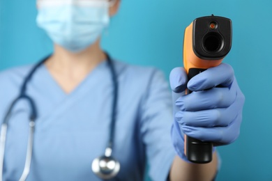 Photo of Doctor with infrared thermometer on blue background, closeup. Checking temperature during Covid-19 pandemic