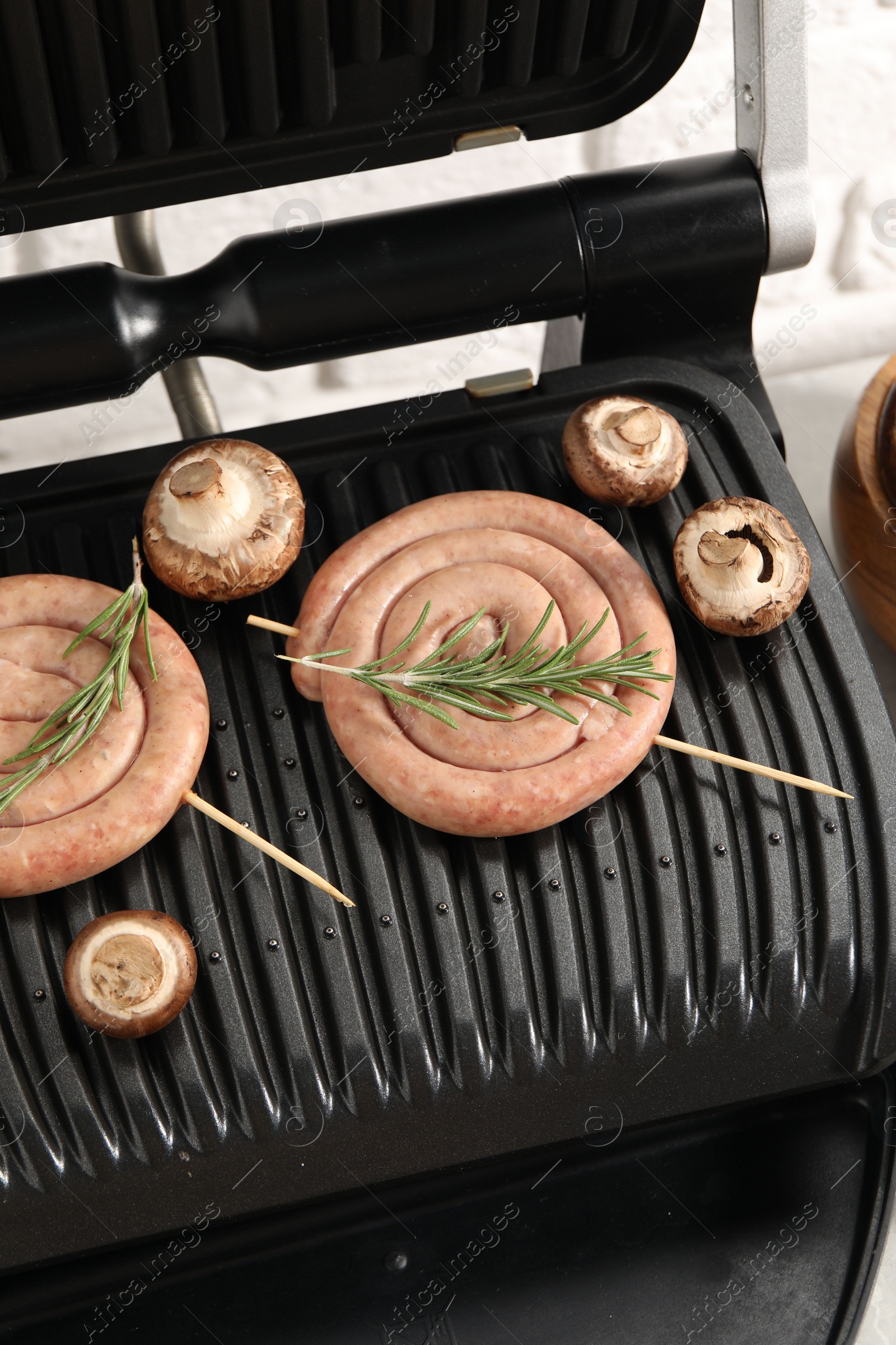 Photo of Electric grill with homemade sausages, rosemary and mushrooms on table, above view