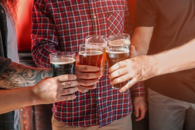 Group of friends clinking glasses with beer on color background