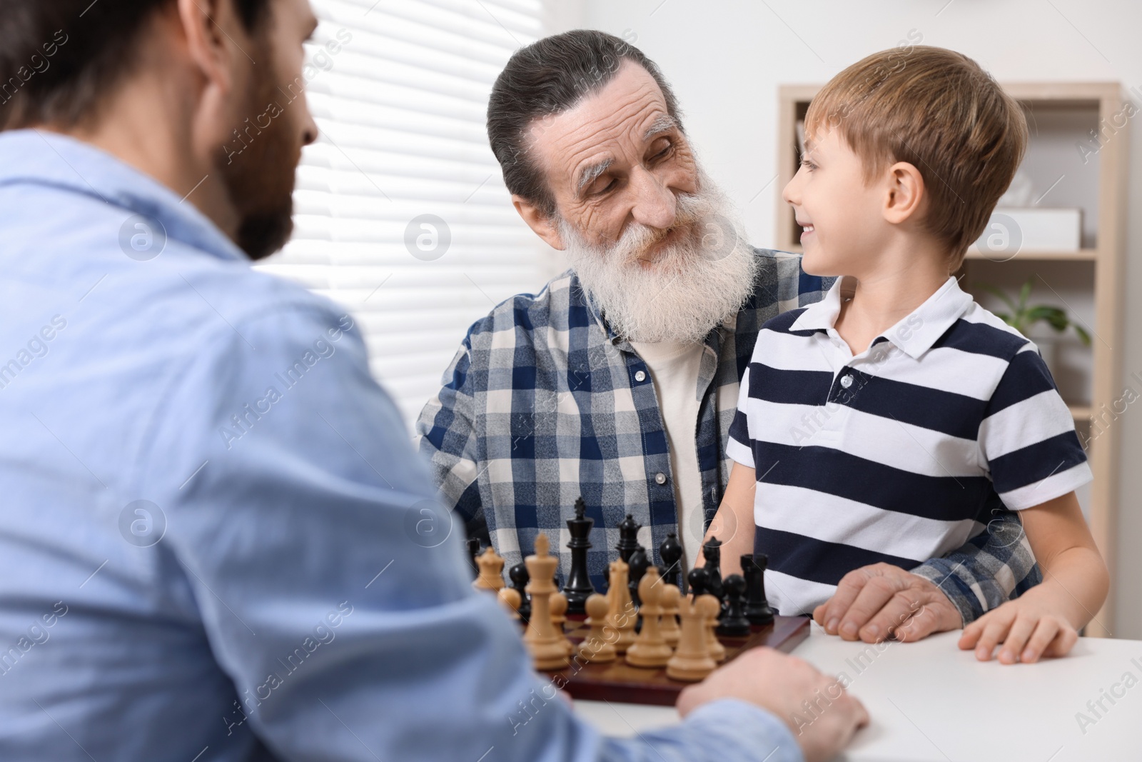 Photo of Family playing chess together at table in room