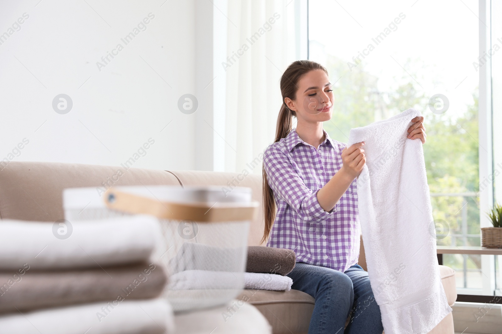 Photo of Happy young woman with clean towel on sofa indoors. Laundry day