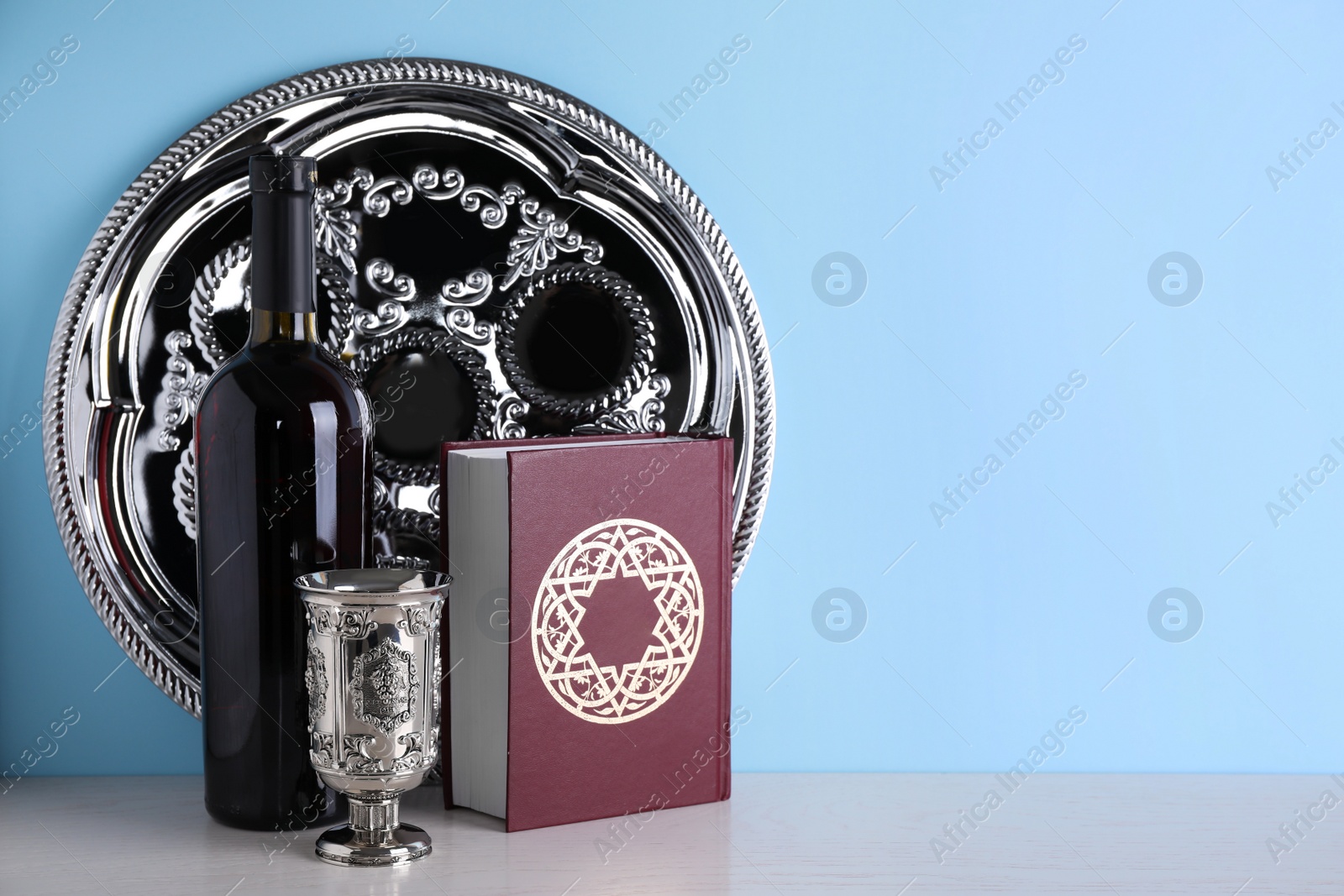 Photo of Symbolic Pesach (Passover Seder) items on table against light blue background, space for text