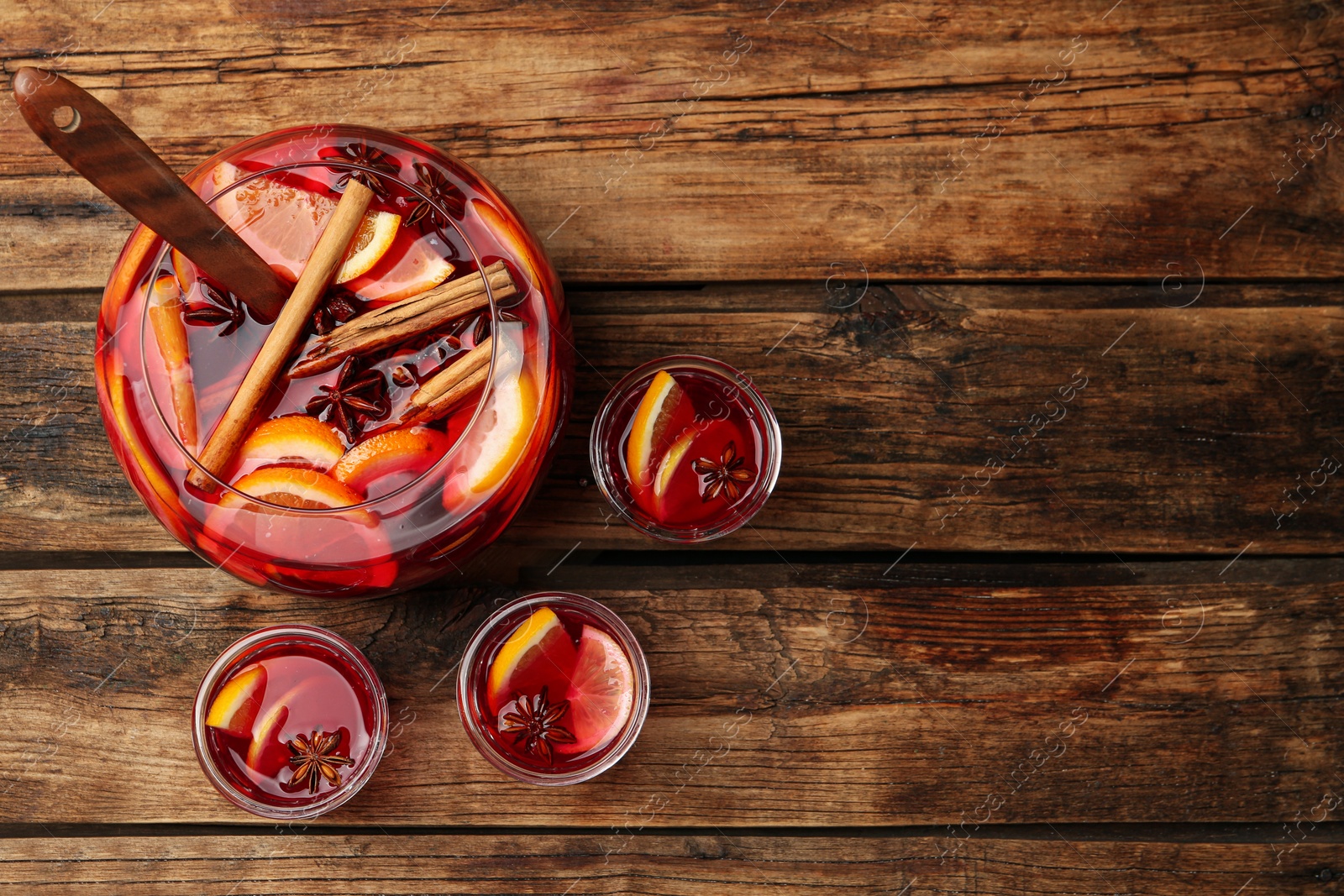 Photo of Glasses and bowl of delicious aromatic punch drink on wooden table, flat lay. Space for text