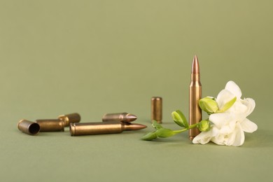 Photo of Bullets, cartridge cases and beautiful freesia flowers on olive background