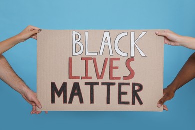 People holding sign with phrase Black Lives Matter on light blue background, closeup. Racism concept
