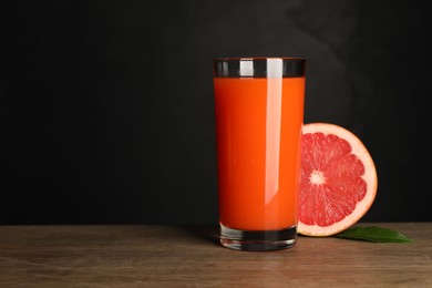 Photo of Tasty grapefruit juice in glass, leaf and fresh fruit on wooden table against black background. Space for text