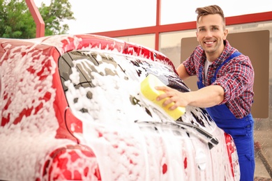 Male worker cleaning vehicle with sponge at car wash