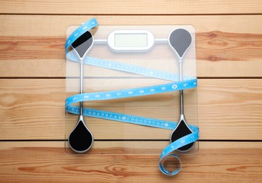 Bathroom scale and measuring tape on wooden floor, top view. Weight loss concept