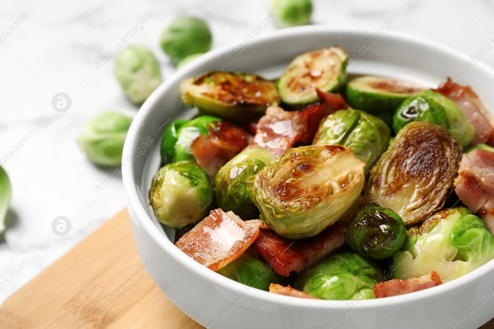 Photo of Delicious Brussels sprouts with bacon in bowl on light table, closeup