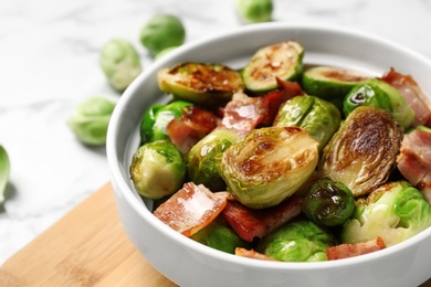 Delicious Brussels sprouts with bacon in bowl on light table, closeup