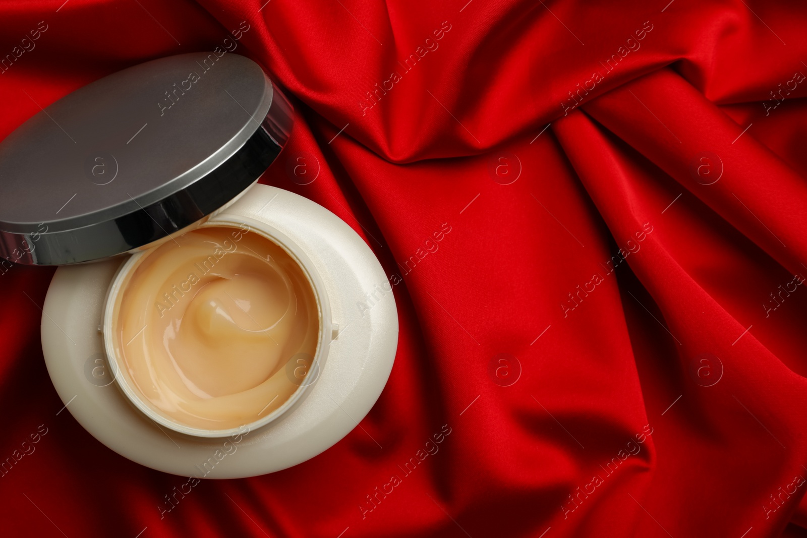 Photo of Open jar of hair care cosmetic product on red fabric, top view. Space for text