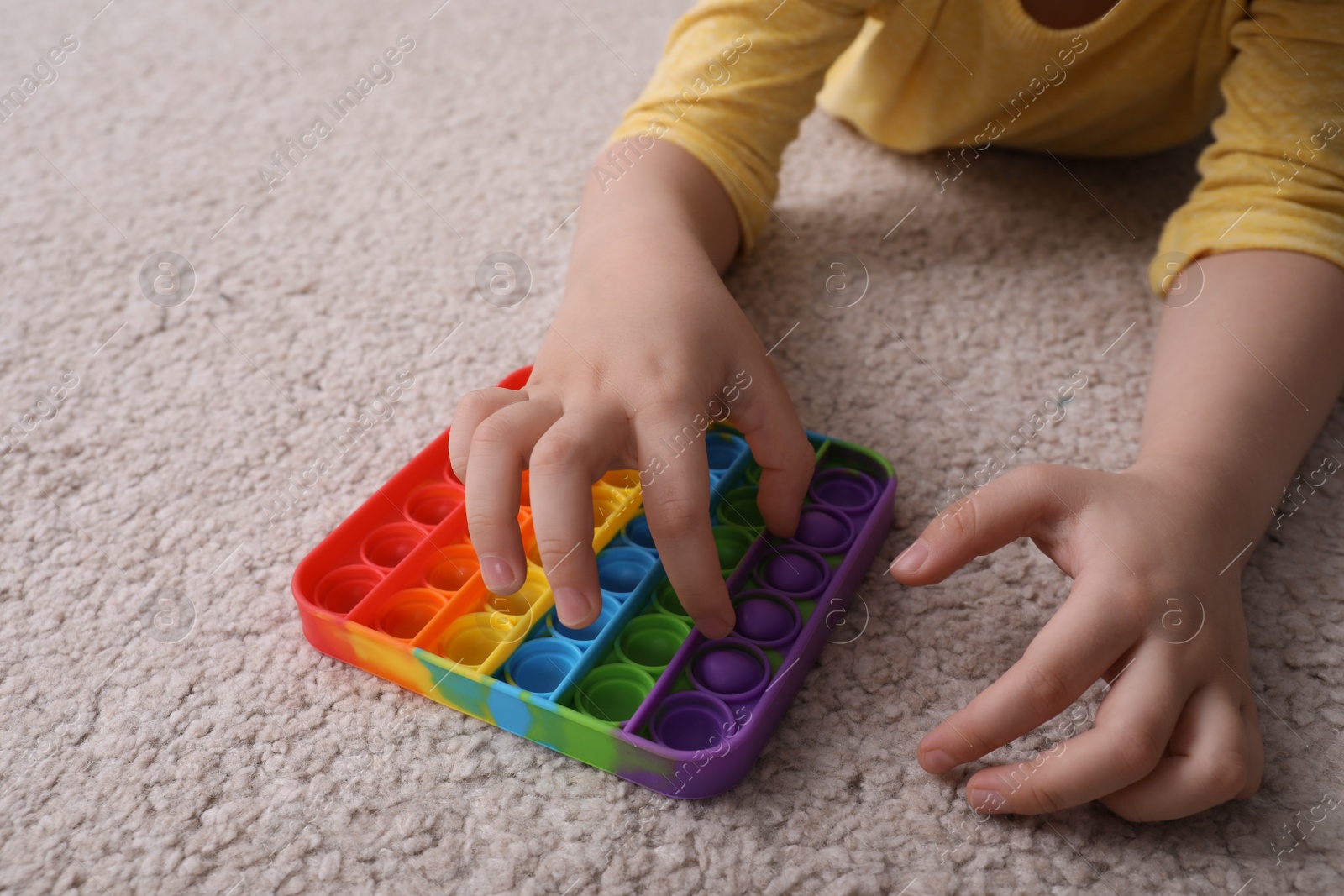 Photo of Little boy playing with pop it fidget toy on floor, closeup