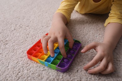 Little boy playing with pop it fidget toy on floor, closeup