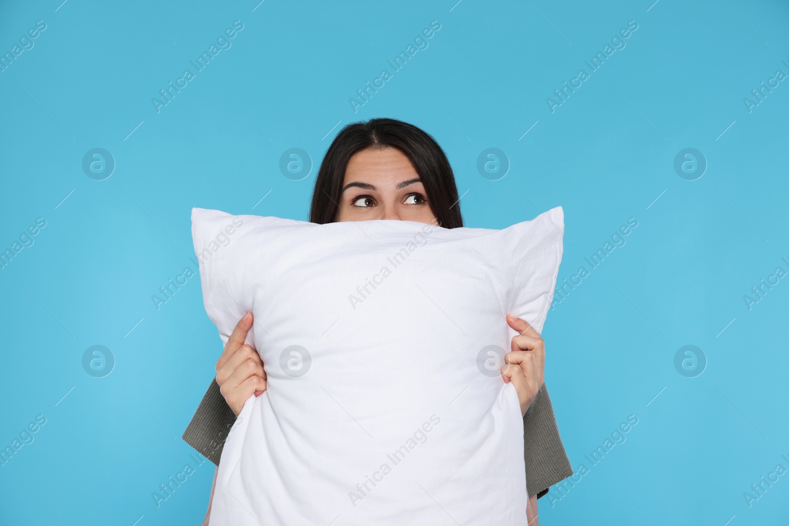 Photo of Young woman covering face with soft pillow on light blue background