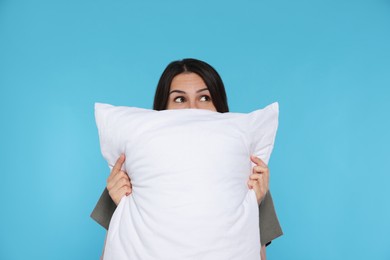 Young woman covering face with soft pillow on light blue background