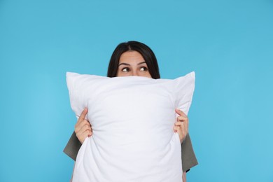 Photo of Young woman covering face with soft pillow on light blue background