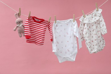 Photo of Different baby clothes and bunny toy drying on laundry line against pink background