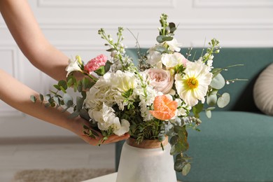 Woman arranging bouquet of beautiful flowers in vase indoors, closeup