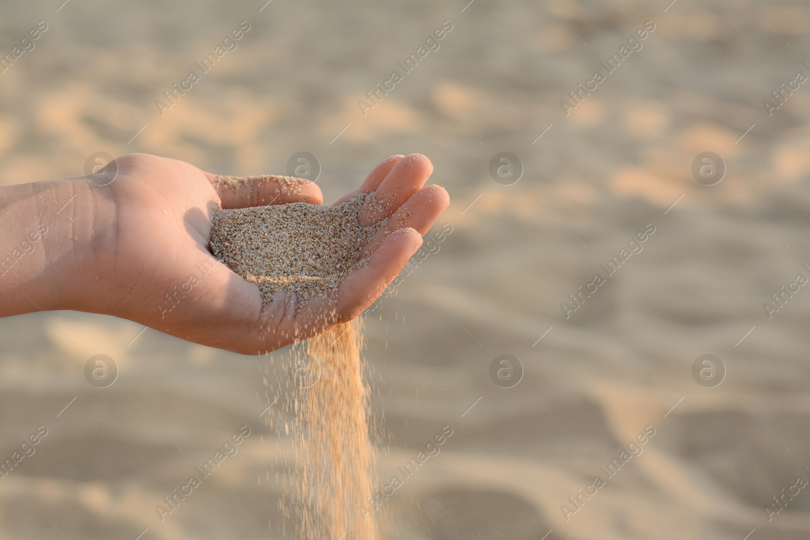 Photo of Girl pouring sand from hand outdoors, closeup. Fleeting time concept