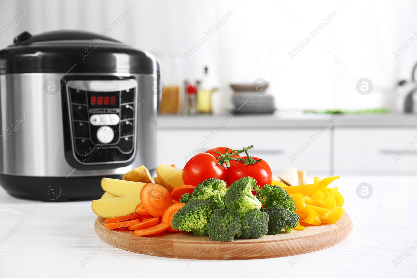 Photo of Wooden board with vegetables and modern multicooker on white table in kitchen. Space for text