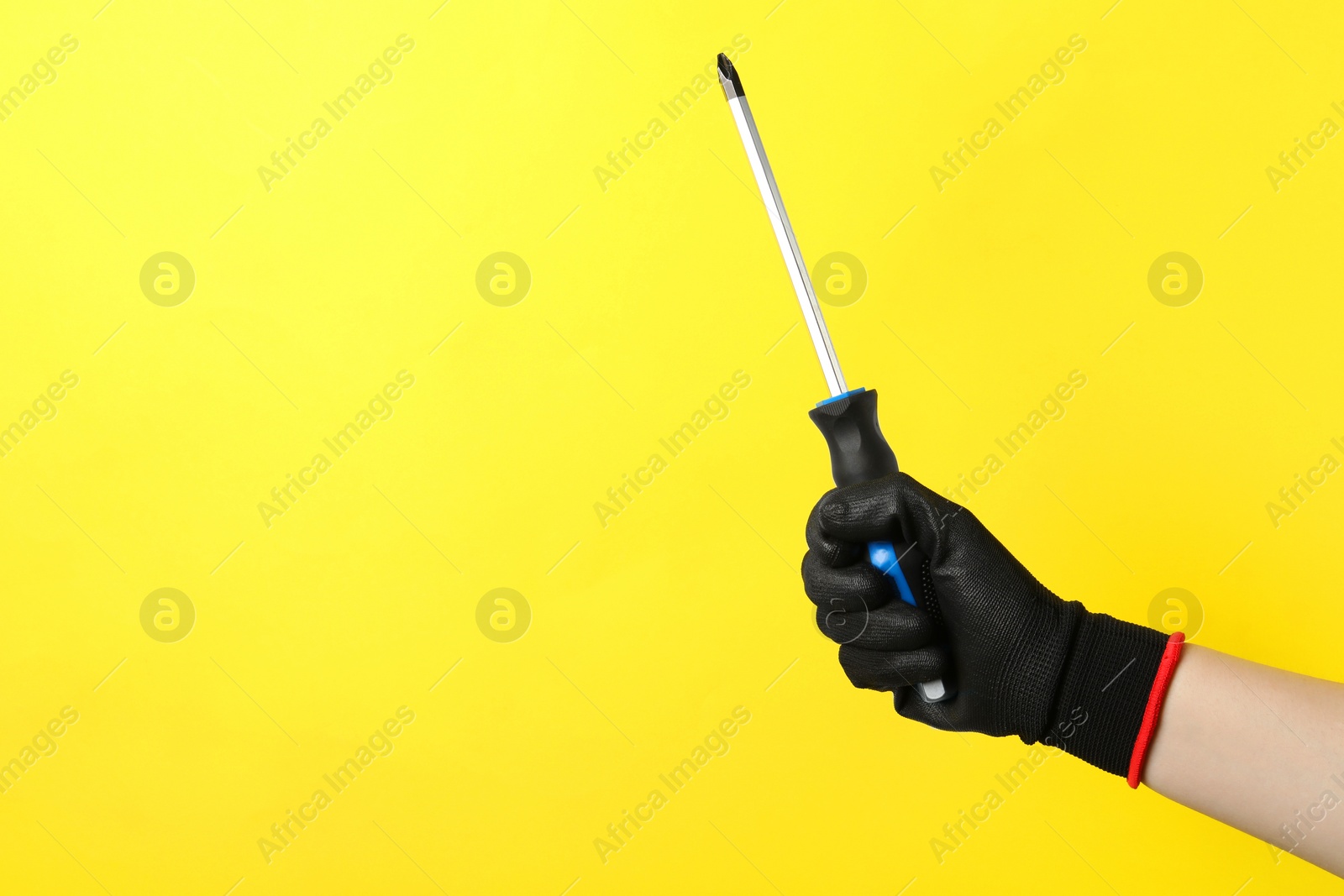 Photo of Woman holding screwdriver on yellow background, closeup. Space for text