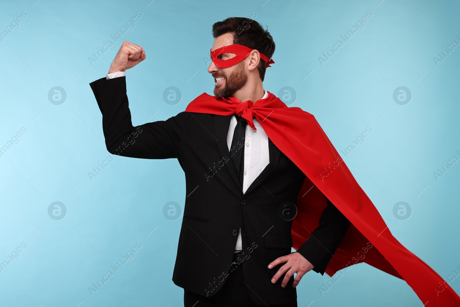 Photo of Businessman wearing red superhero cape and mask on light blue background