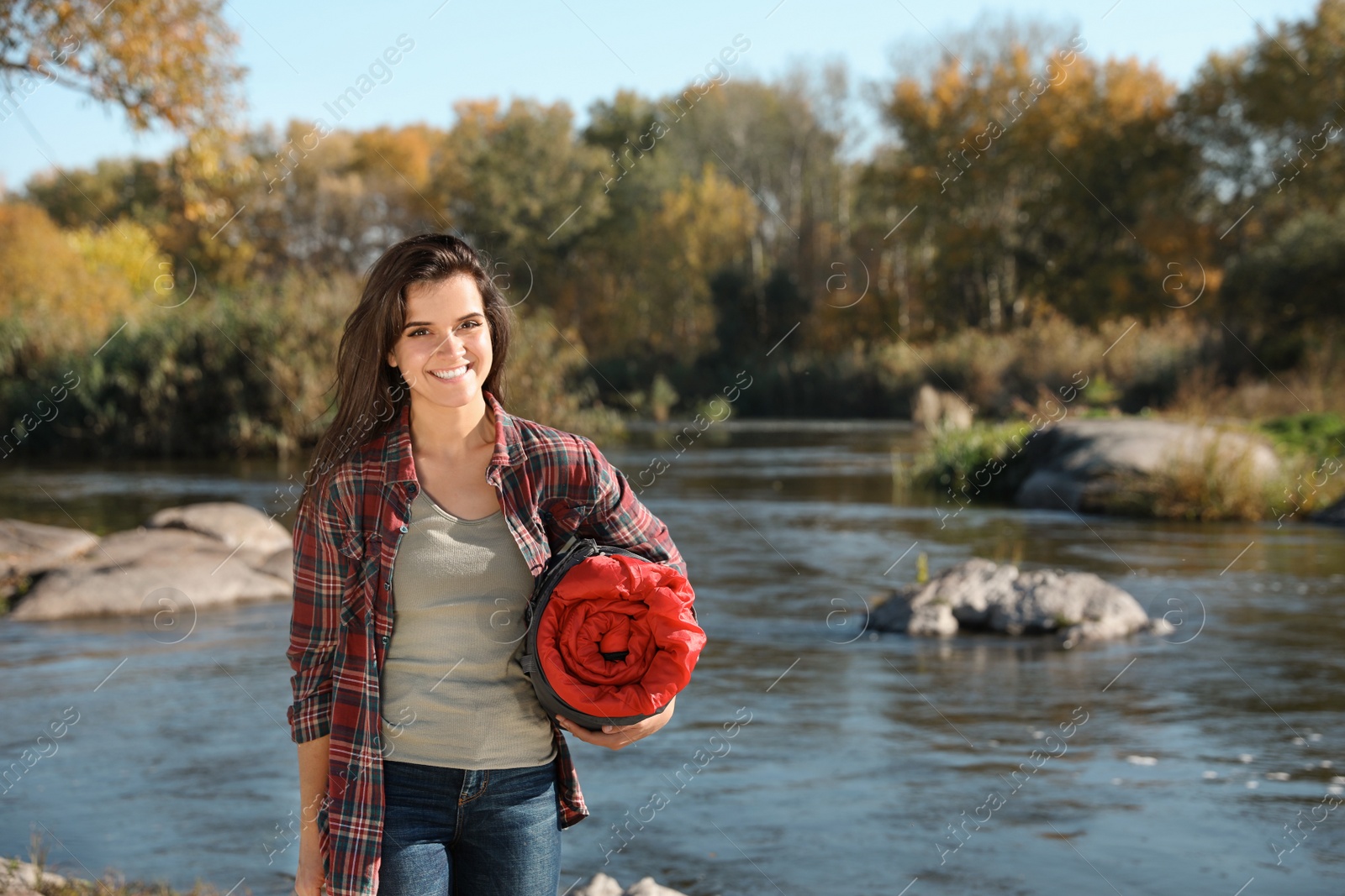 Photo of Female camper with sleeping bag near pond. Space for text