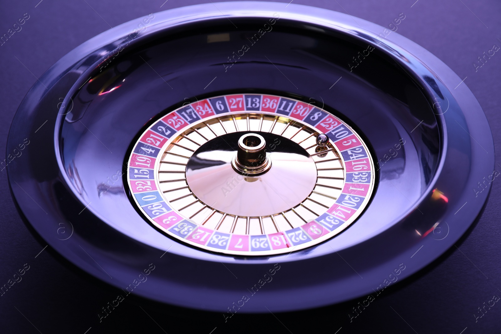 Photo of Roulette wheel with ball on dark violet background, closeup. Casino game