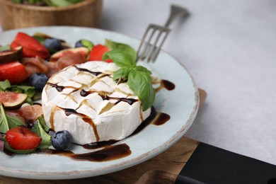Photo of Plate of delicious salad with brie cheese, berries and balsamic vinegar on light grey table, closeup. Space for text