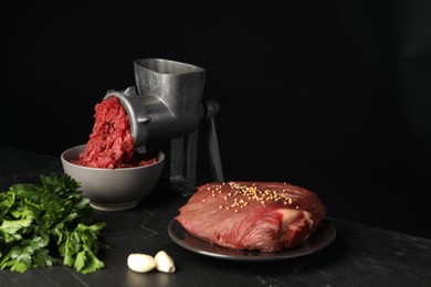 Photo of Metal meat grinder with beef mince and spices on dark textured table against black background. Space for text