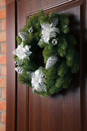 Beautiful Christmas wreath with festive decor hanging on wooden door