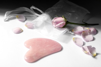 Photo of Rose quartz gua sha tool and flower on white table