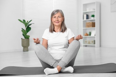 Photo of Happy senior woman practicing yoga on mat at home