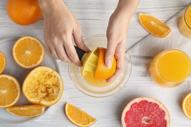 Woman squeezing orange juice at wooden table, top view