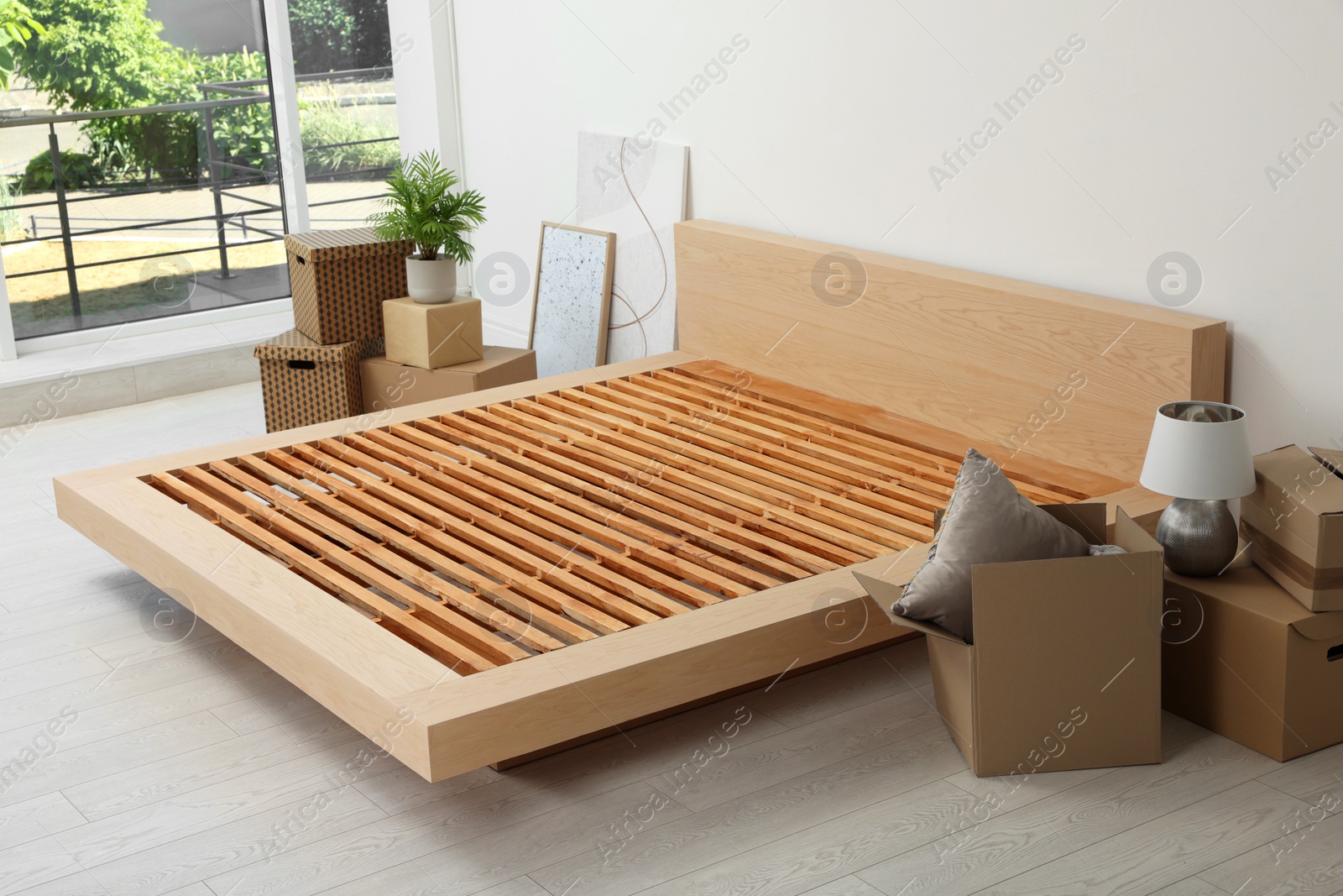 Photo of New wooden bed frame, moving boxes and decor elements indoors