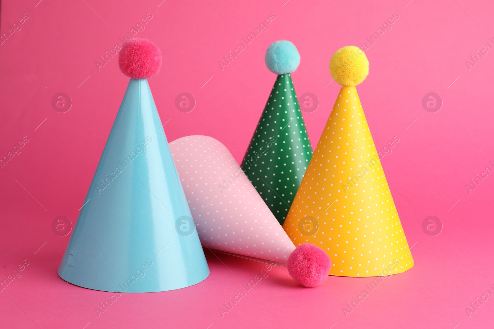 Photo of Beautiful party hats with pompoms on pink background