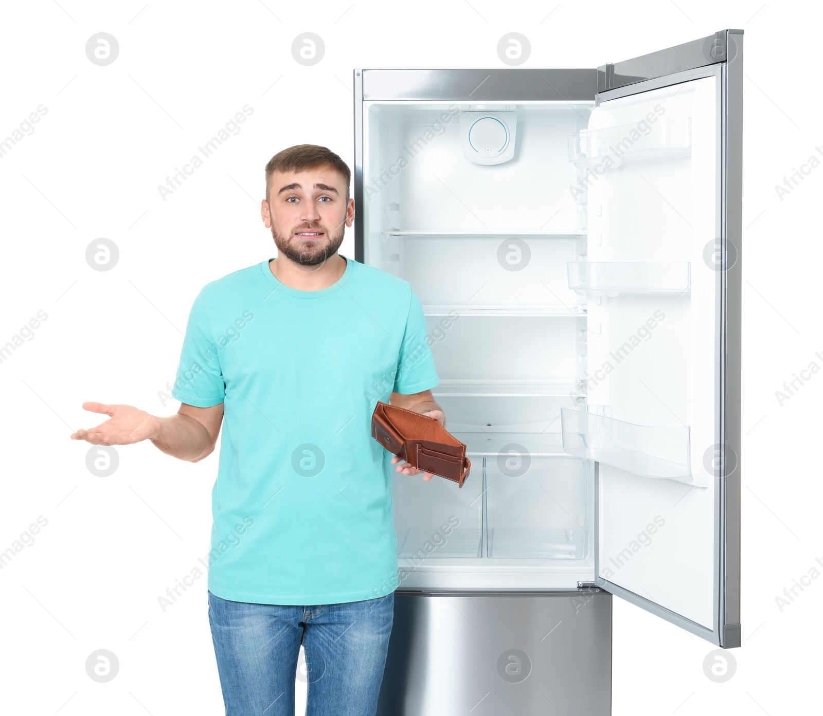 Photo of Young man with no money in wallet near empty refrigerator on white background