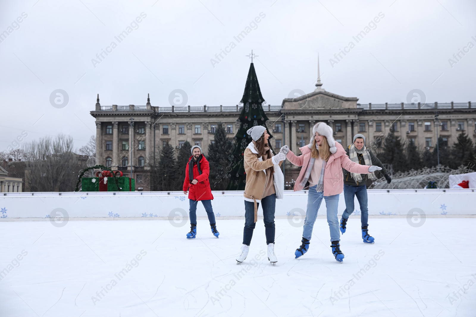 Image of Happy friends skating along ice rink outdoors