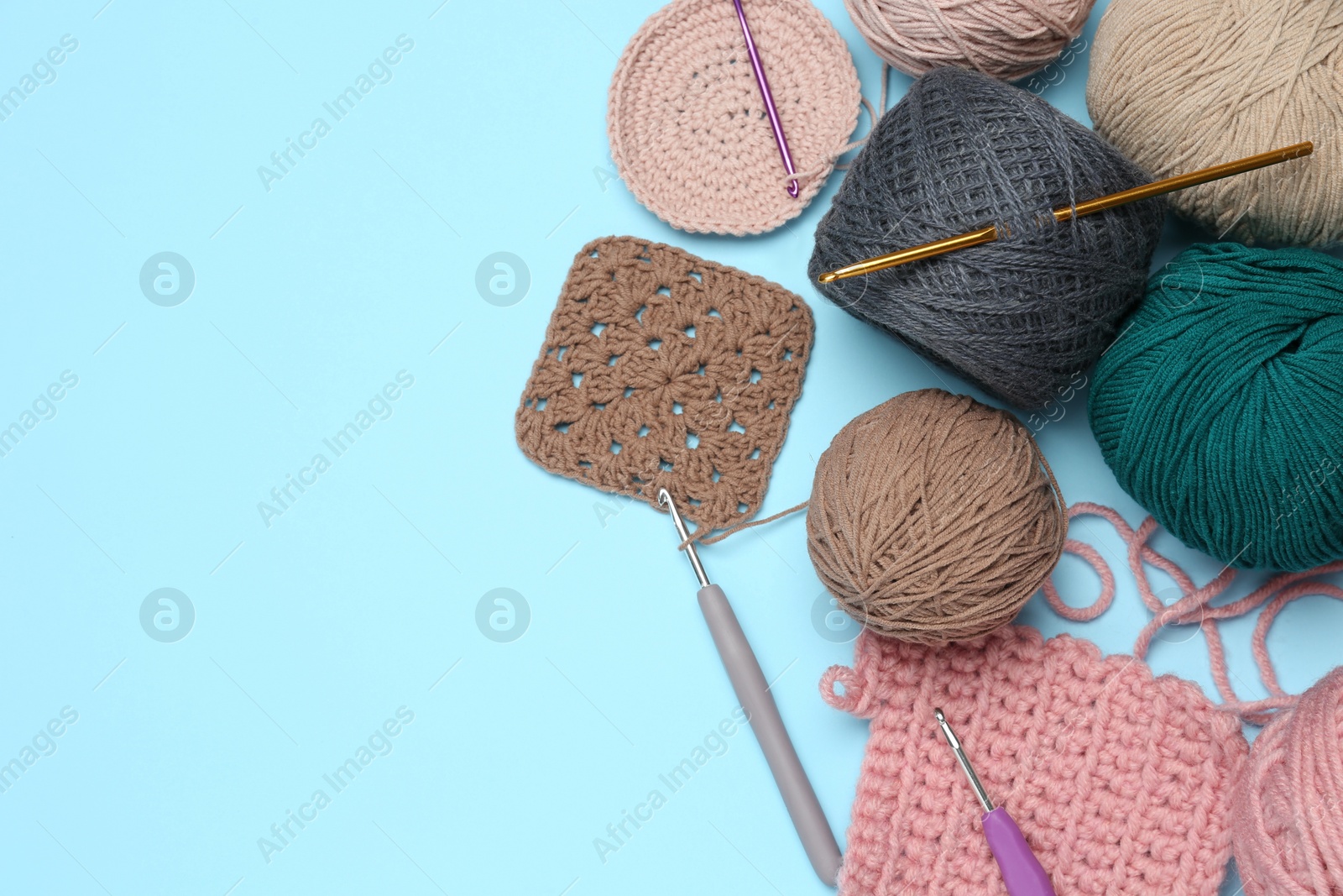 Photo of Clews, knitting and crochet hooks on light blue background, flat lay. Space for text