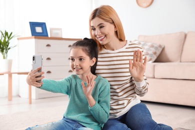 Photo of Mother and her daughter using video chat on smartphone at home