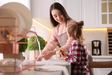 Photo of Mother and daughter washing dishes together in kitchen at home