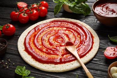 Composition with pizza crust and ingredients on dark wooden table