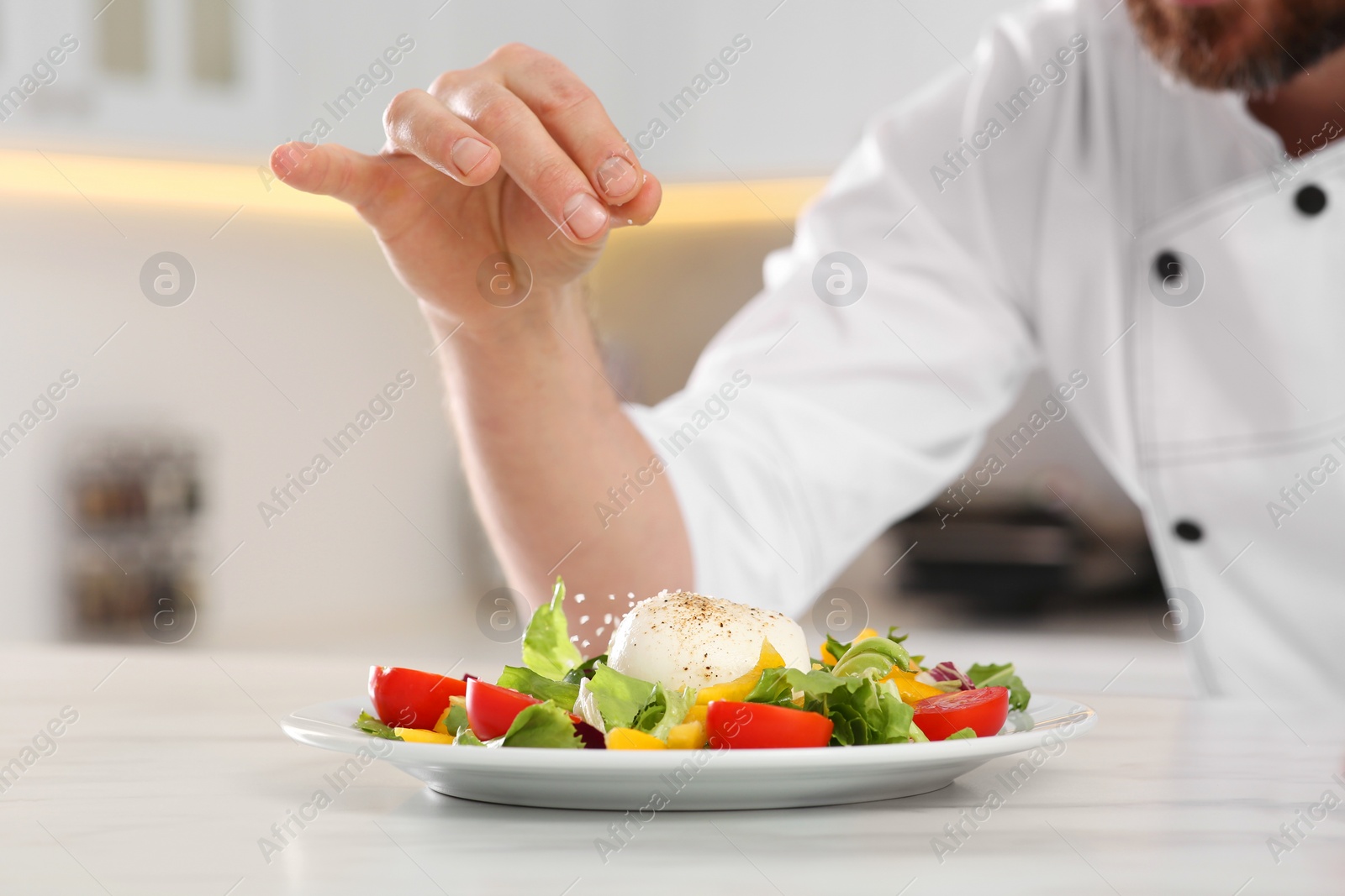 Photo of Professional chef salting delicious salad at marble table, closeup