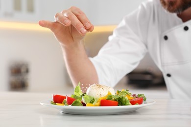 Professional chef salting delicious salad at marble table, closeup