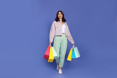 Beautiful young woman with paper shopping bags on purple background