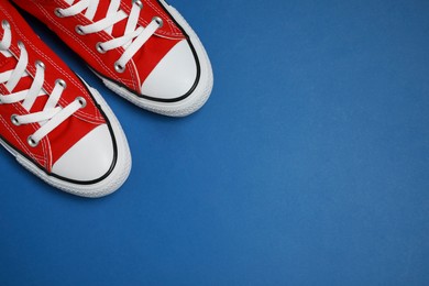 Photo of Pair of new stylish red sneakers on blue background, flat lay. Space for text