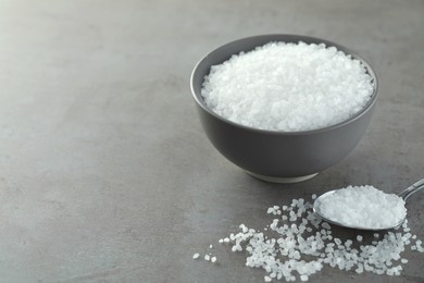 Photo of Bowl and spoon with natural sea salt on grey table, space for text